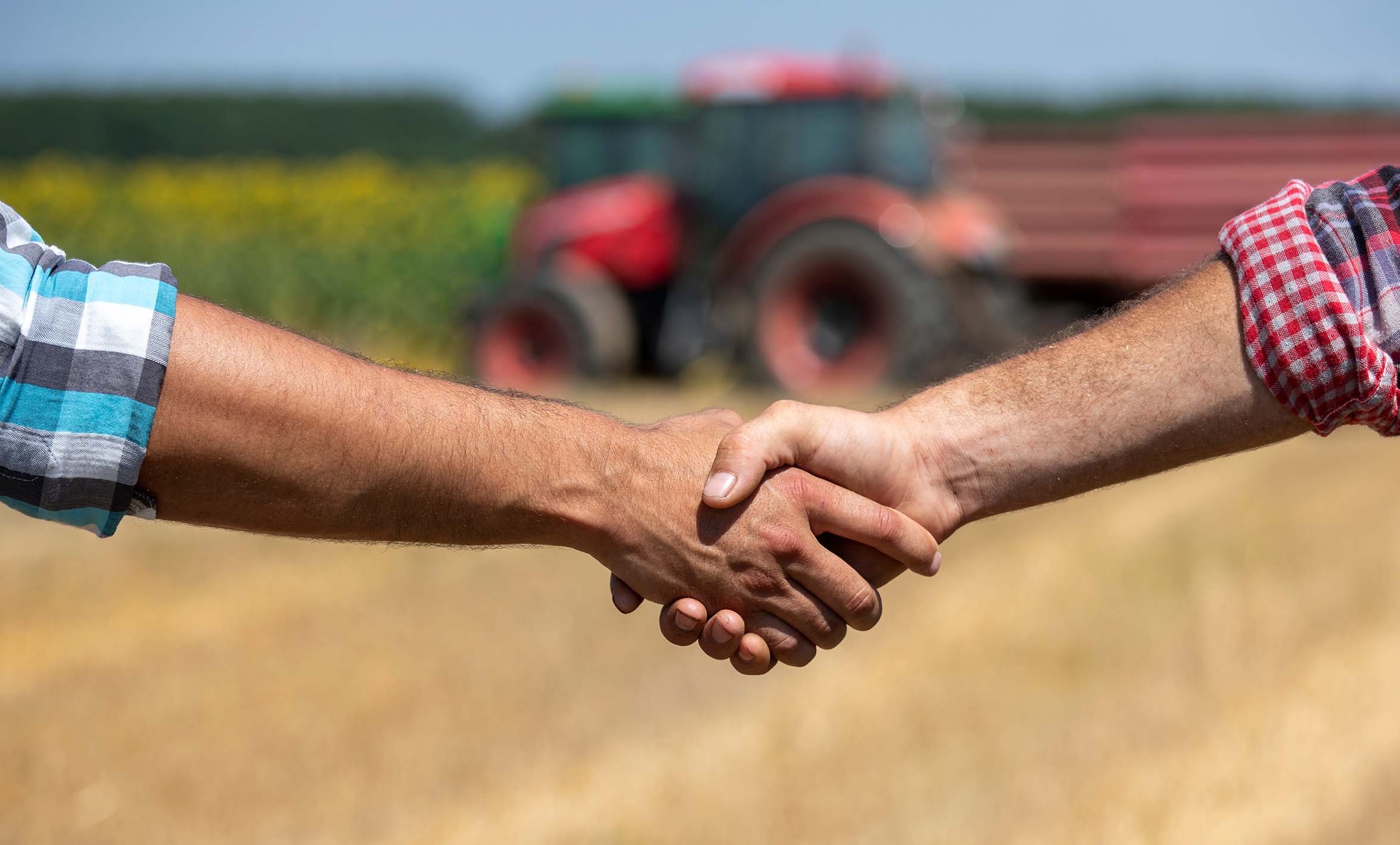 Farmers shaking hands in field in front of tractor with trailer during wheat harvest in summer time
